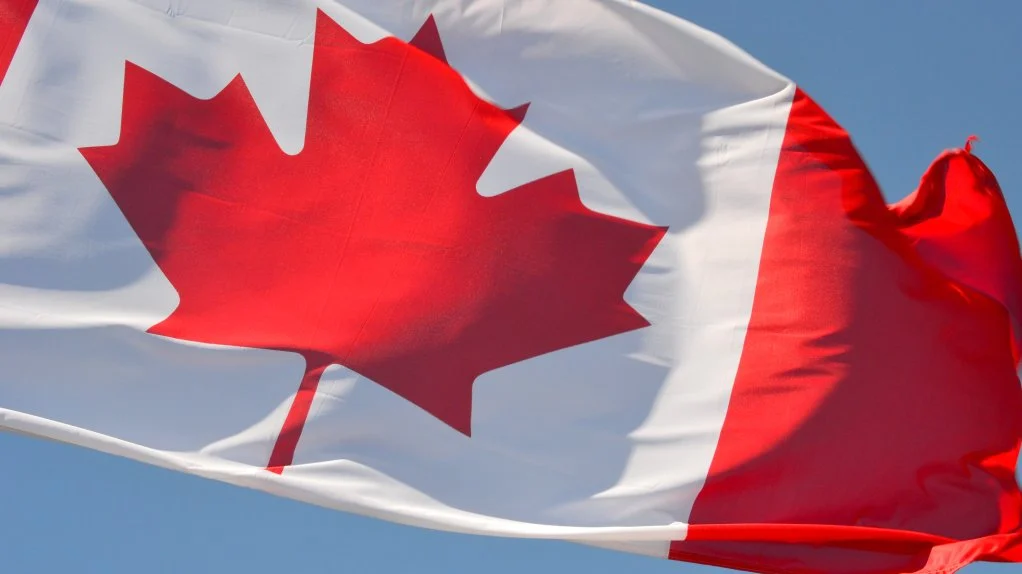 Canadian national flag waving in the wind against a clear blue sky.