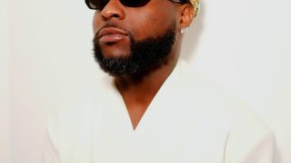 Afrobeats star Davido poses in a white outfit, wearing a jeweled crown and black sunglasses during the promotion of his sixth studio album, ORIADÉ.