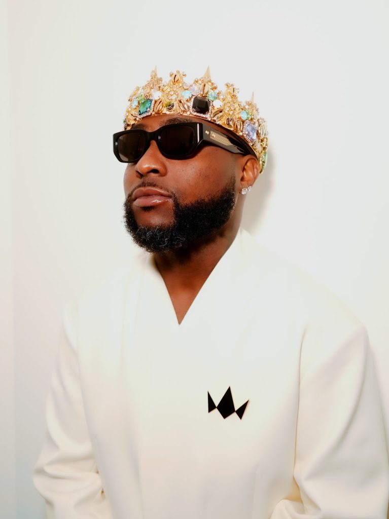 Afrobeats star Davido poses in a white outfit, wearing a jeweled crown and black sunglasses during the promotion of his sixth studio album, ORIADÉ.