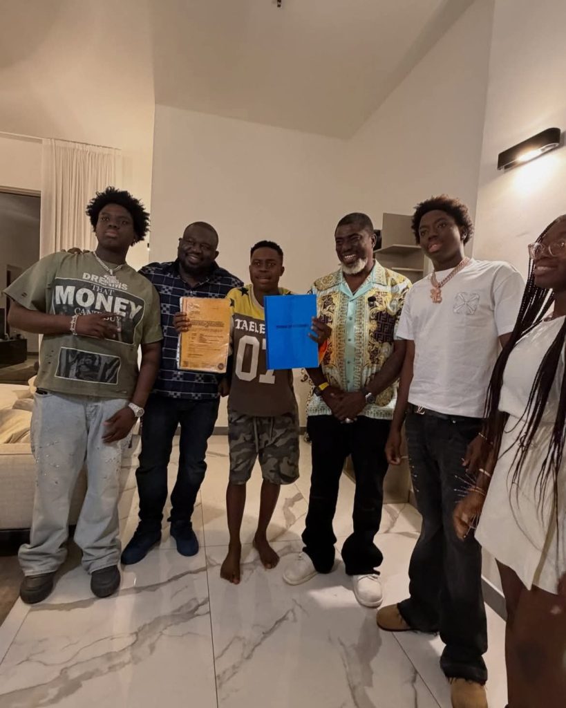 Peller and a group of people pose indoors as he receives property documents, with a man holding a blue folder and another holding a document.