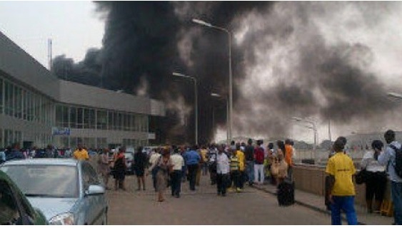 Thick black smoke rises near a terminal building at Murtala Muhammed International Airport in Lagos as passengers and bystanders gather outside during an emergency response.