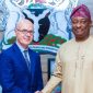 Nigerian Minister of Aviation Festus Keyamo wearing traditional attire shaking hands with a foreign official in front of the Nigerian Coat of Arms.