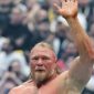 Brock Lesnar raises his right hand to acknowledge the crowd inside a packed WWE arena following a match, with fans blurred in the background.