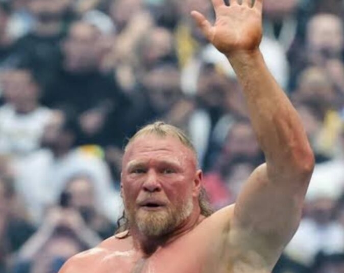 Brock Lesnar raises his right hand to acknowledge the crowd inside a packed WWE arena following a match, with fans blurred in the background.