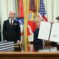 US President Donald Trump holds up a signed executive order on birthright citizenship at the White House, with officials standing nearby.