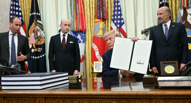 US President Donald Trump holds up a signed executive order on birthright citizenship at the White House, with officials standing nearby.